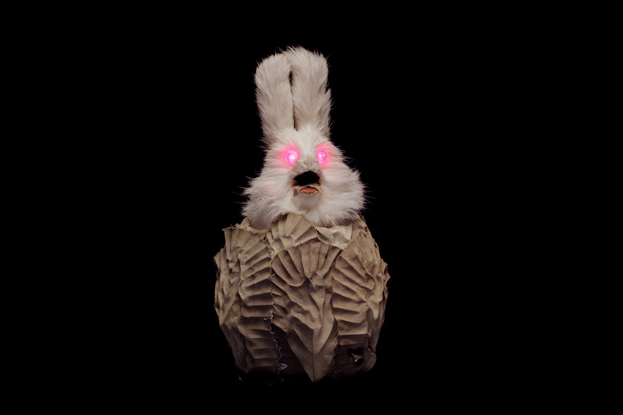 Ein Hase mit pink leuchtenden Augen und gewellten Tüchern am Körper vor schwarzem Hintergrund