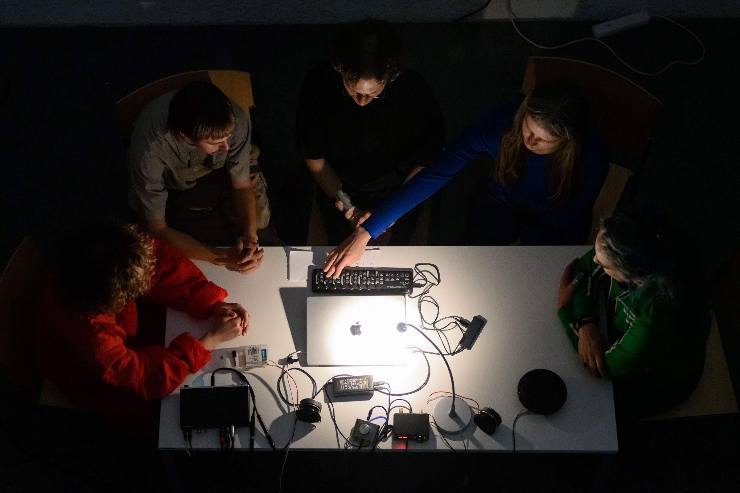 Fünf Personen sitzend bei einem Schreibtisch mit Lampe und Technik