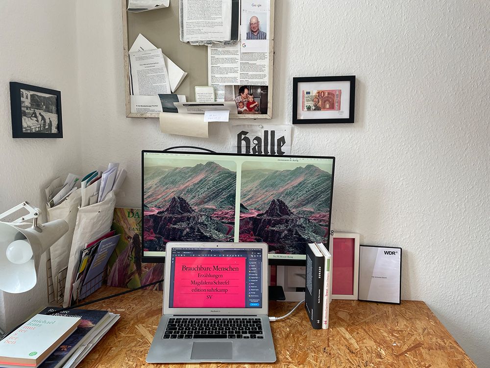 Schreibtisch mit Laptop, Bildschirm und Zettelwerk