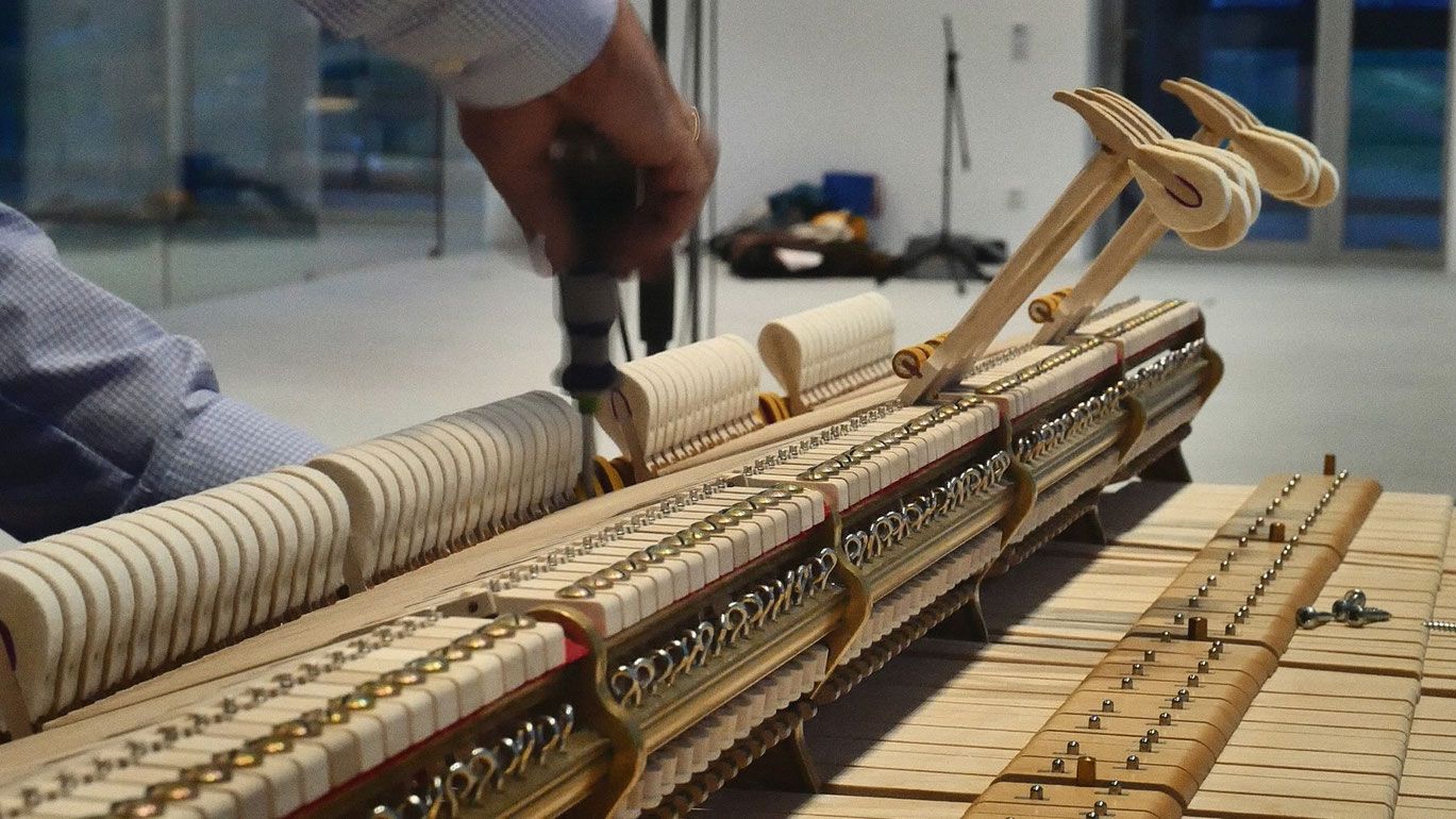 Innenbau von einem Klavier am Boden und Hände, die daran rumschrauben