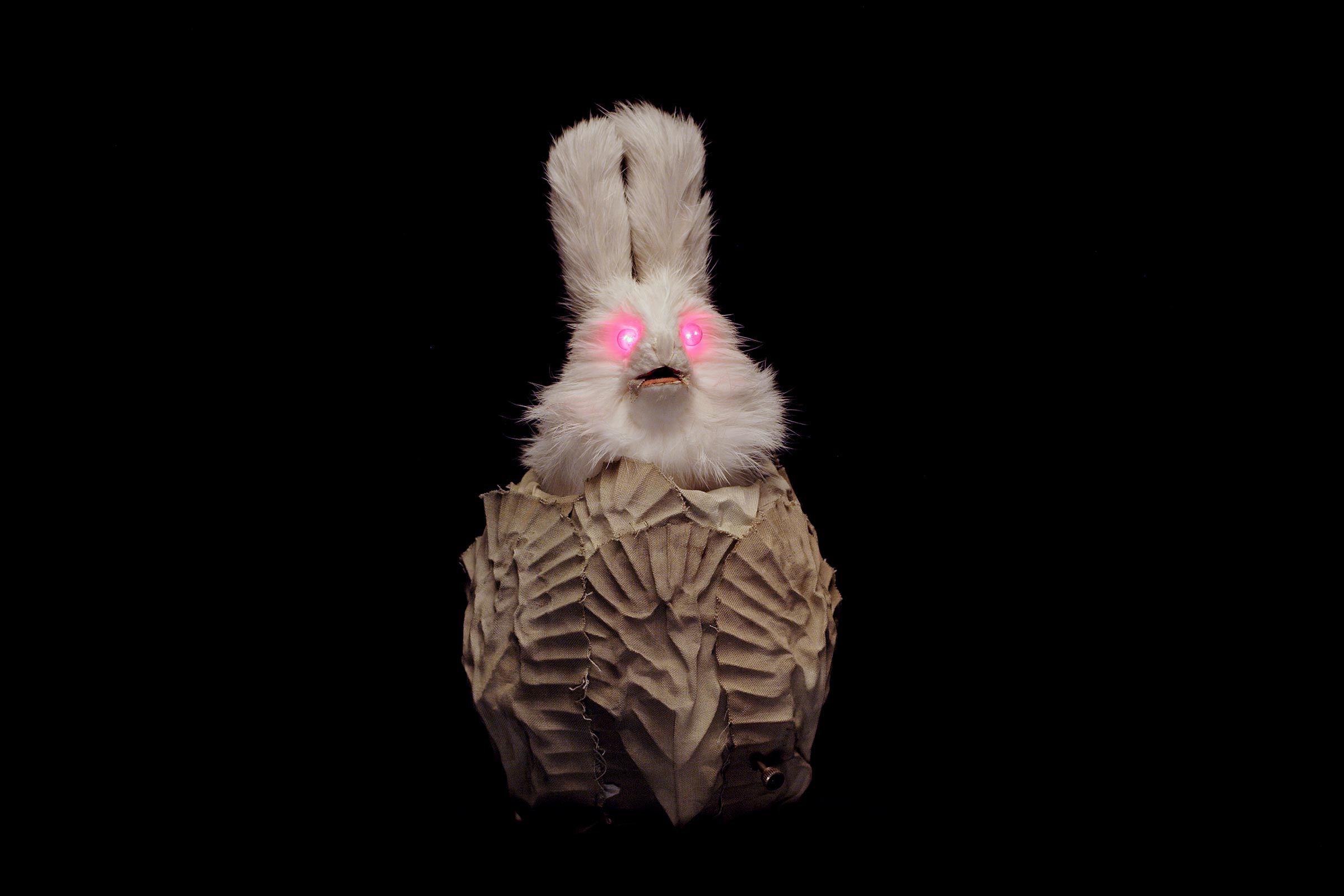 Ein Hase mit pink leuchtenden Augen und gewellten Tüchern am Körper vor schwarzem Hintergrund