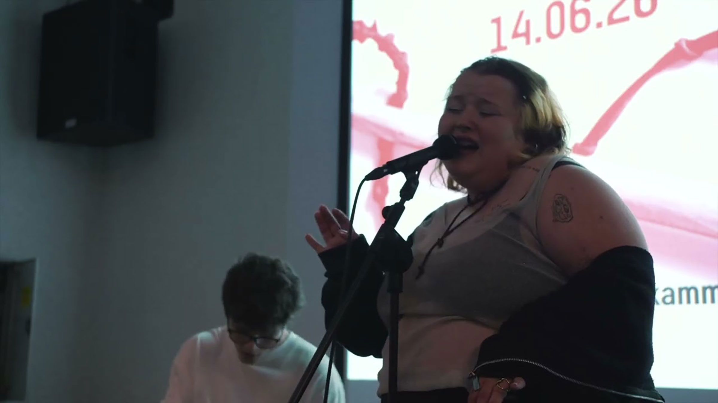 Frau singt in ein Mikrofon, mit einem Mann hinter ihr